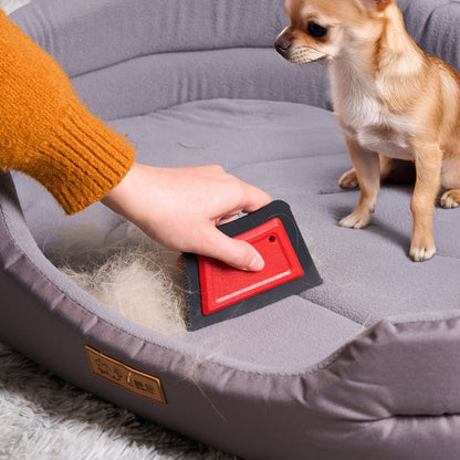 Hand dragging the pet hair remover pad across a pet bed, raking fur into a pile